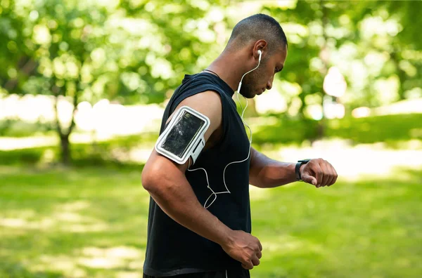 Πλευρική άποψη του Αφροαμερικανού τύπου τον έλεγχο των δεδομένων υγείας για SmartWatch μετά από τρέξιμο στο πάρκο — Φωτογραφία Αρχείου