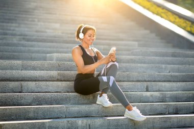 Güzel siyah kadın koşucu parkta merdivenlerde oturuyor.