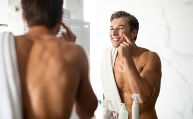 Aynaya bakan yakışıklı adam krem sürüyor.