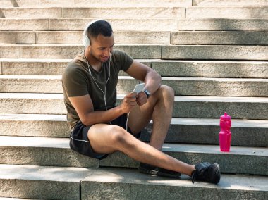 Kulaklıklı ve cep telefonlu mutlu siyah adam merdivenlerde dinleniyor ve eğitimden sonra müzik dinliyor.