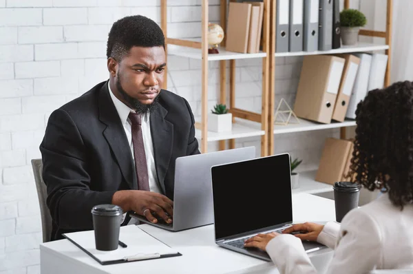 Konflikt på arbeidsplassen. Misfornøyd afroamerikaner som har uenighet med sin kvinnelige kollega på kontoret, fritt rom – stockfoto