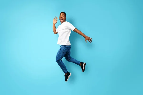 Afro-Amerikaanse man schreeuwen springen in de lucht over blauwe achtergrond — Stockfoto