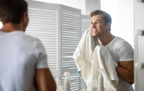 Självsäker ung man tittar i spegeln med handduk — Stockfoto