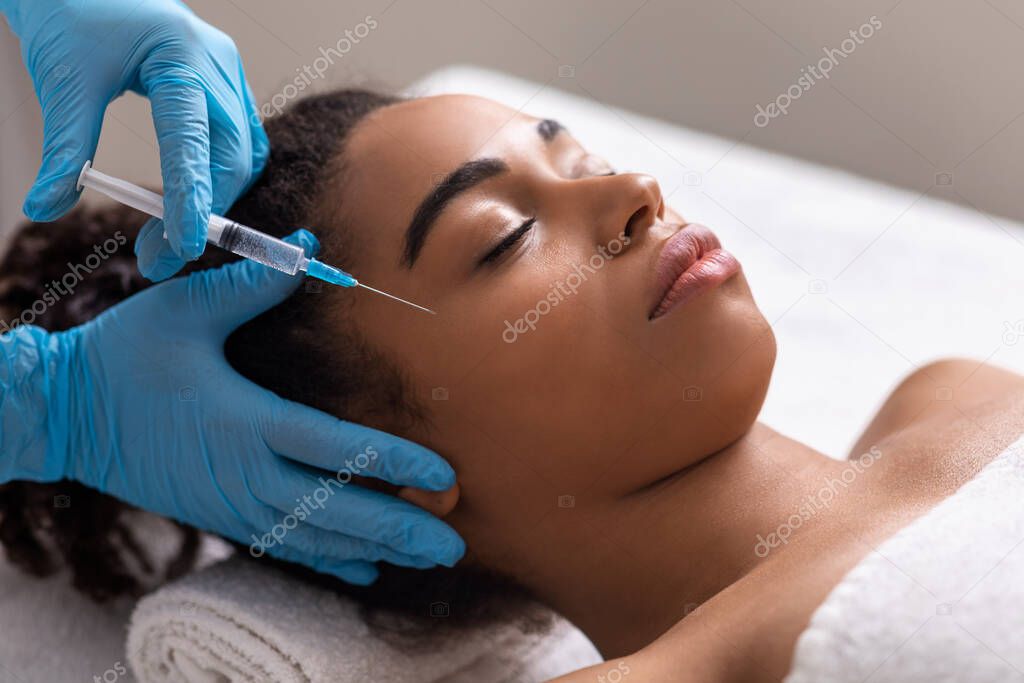 Young black lady receiving eye zone injection at beauty salon