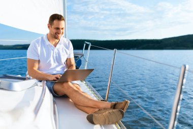 Yatta oturan mutlu adam dizüstü bilgisayarla yelkenlide çalışıyor.