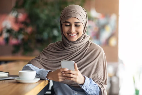 微笑的穆斯林女人喝着长颈鹿，在咖啡店用电话 — 图库照片