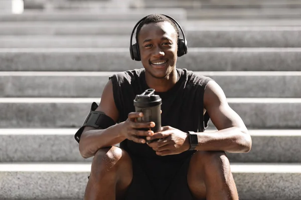 Černoch odpočívá po běhání venku, poslouchá hudbu a má proteinový nápoj — Stock fotografie