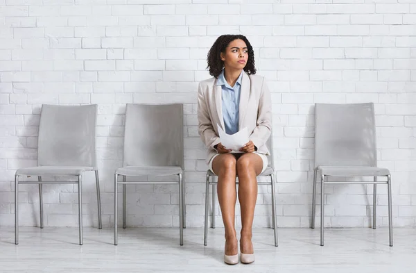 Worried black woman with CV waiting for work interview at company hall, blank space