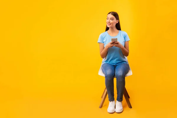 Studio shot van meisje zitten op stoel met telefoon — Stockfoto