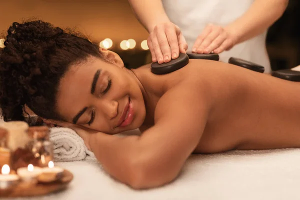 Senhora africana recebendo massagem profissional de pedra quente no spa — Fotografia de Stock