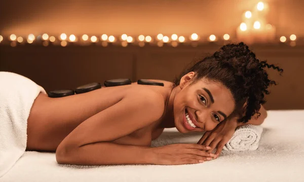 Happy african american woman enjoying hot stone massage at spa — Stock Photo, Image