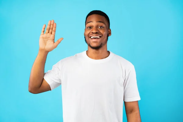 Fröhlicher Afrikaner winkt mit der Hand, Hallo-Gruß über blauem Hintergrund — Stockfoto