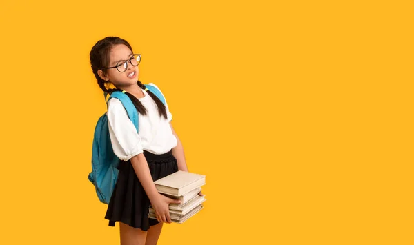 Descontenta asiática escuela chica llevando pesado libros sobre amarillo fondo — Foto de Stock