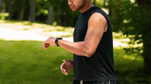 Unerkennbarer schwarzer Sportler checkt seine Smartwatch während seines Laufs im Park, leerer Raum — Stockfoto