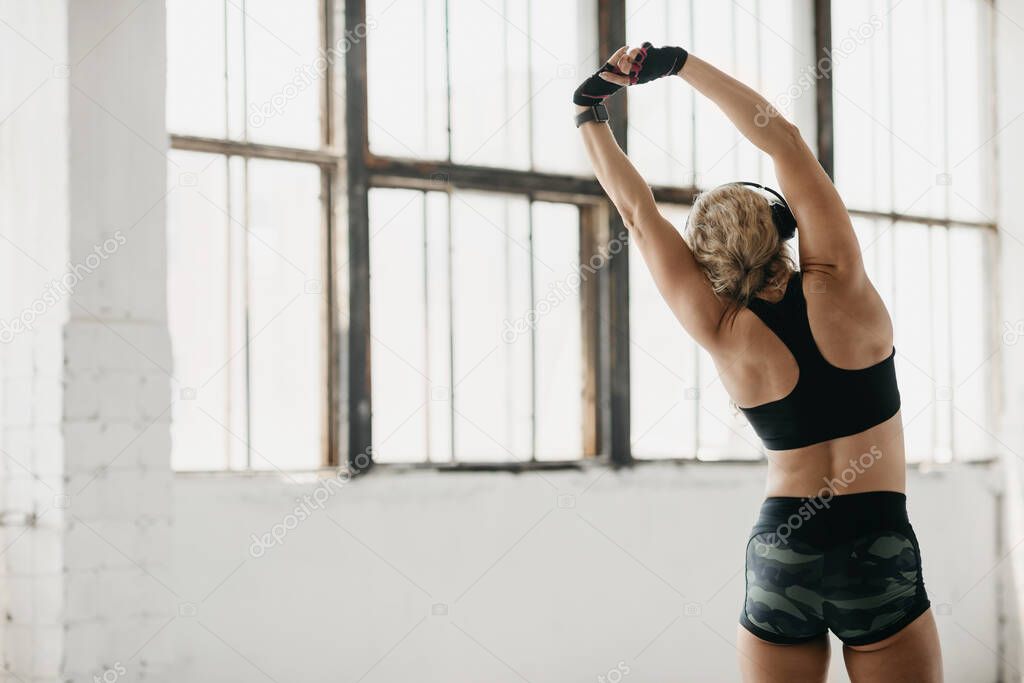 Stretching and motivation. Muscular woman in sportswear with fitness tracker and headphones doing exercises
