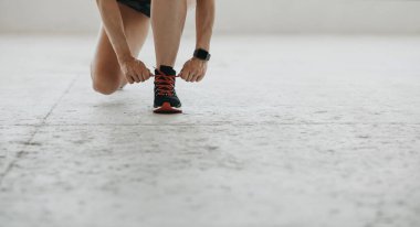 Maratona hazırlanıyorum. Akıllı saatli bir kadın ayakkabı bağcıklarını spor ayakkabılarına bağlıyor, yerde oturuyor.