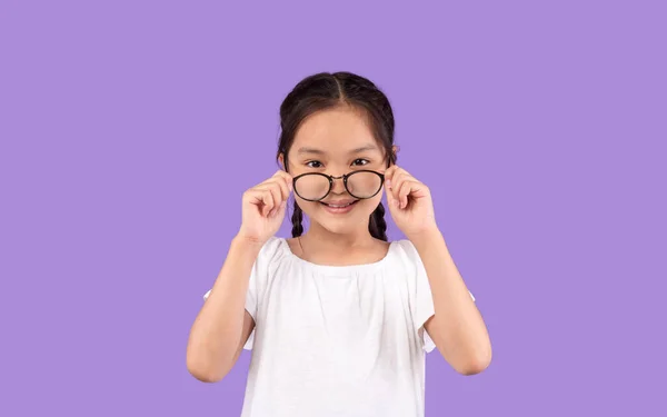 Aziatisch klein meisje op zoek naar camera boven glazen, studio schot — Stockfoto
