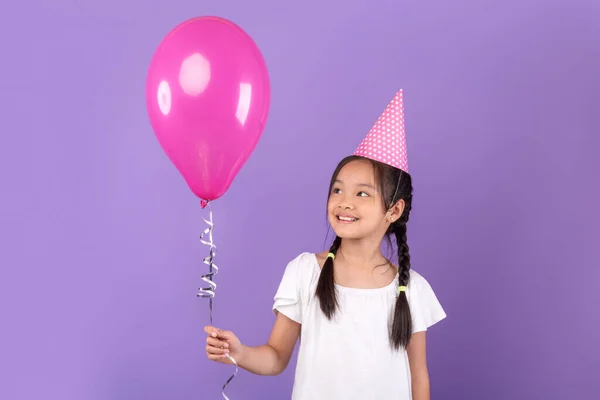 Lächelndes koreanisches Mädchen trägt Geburtstagsmütze mit Luftballon, lila Hintergrund — Stockfoto