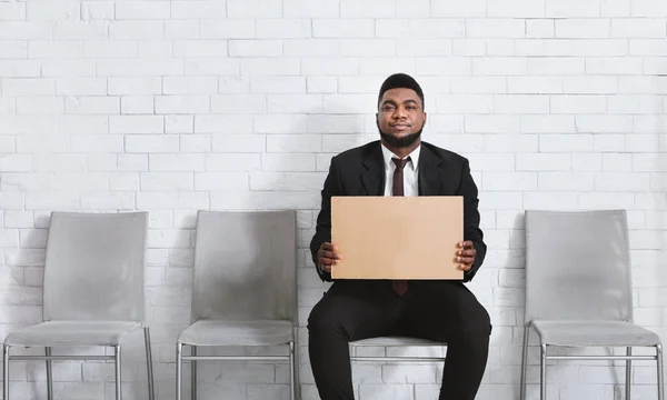 Un homme noir sérieux au bureau porte une pancarte vierge dans le hall de l'entreprise, attendant un entretien d'embauche. Espace de copie — Photo