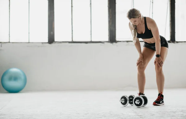 Trött vuxen kvinna i sportkläder med fitness tracker vilar från träning med hantlar i dagsljus — Stockfoto