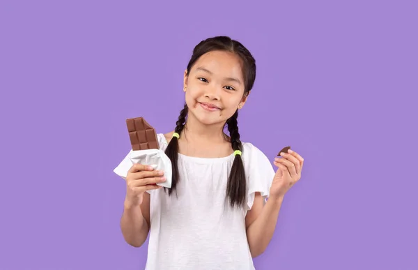 Chica china comiendo chocolate posando sobre fondo púrpura en estudio — Foto de Stock