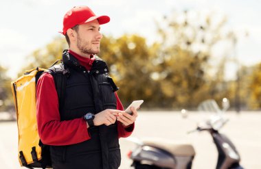 Kurye cep telefonu uygulaması kullanıyor. Dışarıdaki motosiklette yiyecek dağıtıyor.