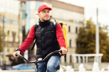 Bisiklette oturan kurye, şehir bölgesinde yiyecek dağıtıyor.
