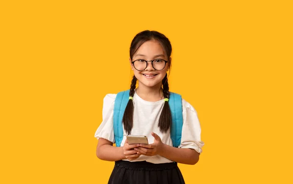 Studentessa cinese utilizzando il telefono cellulare in piedi su sfondo giallo, Studio — Foto Stock