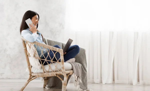Fröhlich asiatisch mädchen relaxing im stuhl, talking auf handy und using laptop — Stockfoto