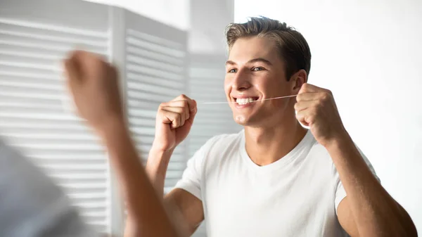 Bello giovane ragazzo utilizzando filo interdentale in bagno — Foto Stock