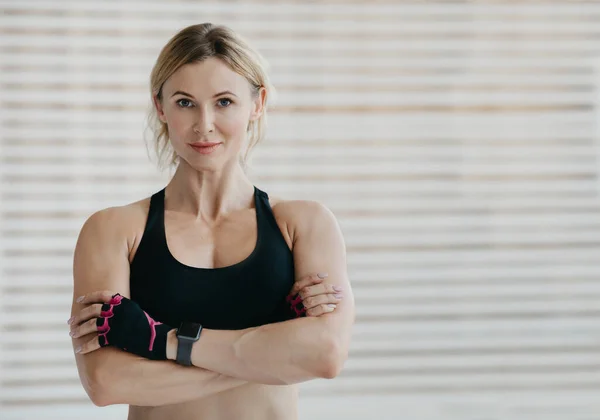 Modelo de fitness y motivación. Mujer amigable con reloj inteligente con los brazos cruzados, demuestra los músculos —  Fotos de Stock