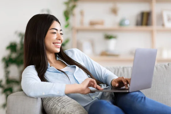 オンラインショッピング。自宅でノートパソコンを使ってアジアの女の子を笑顔,インターネットで購入 — ストック写真