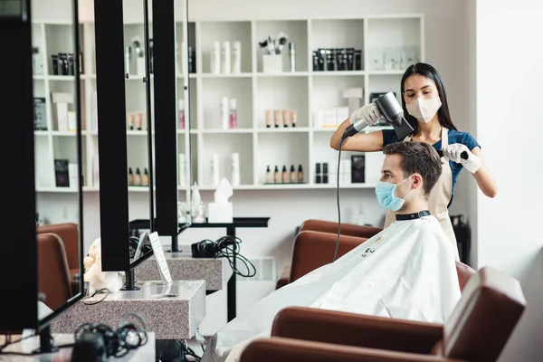 Barbeiro fazendo penteado para cliente masculino, ambos em máscaras médicas — Fotografia de Stock