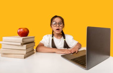 Dizüstü bilgisayardaki Japon liseli kız sarı arka planda oturuyor.