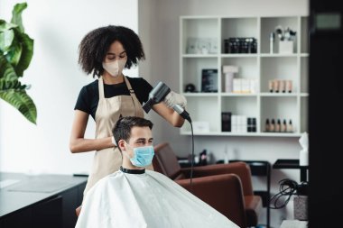 Siyah kuaför müşteri için yeni saç stili yapıyor, hem koruyucu maskeli.