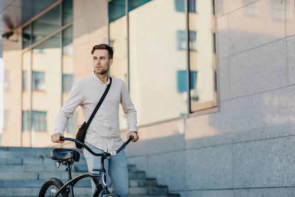 Snel eco-stadsvervoer. Ernstige jonge man in zakelijke kleding, wandelingen met de fiets in de stad — Stockfoto