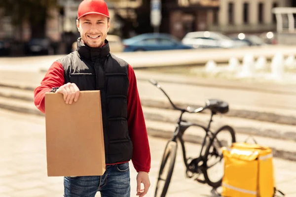 Futár Guy holding Package Mosolyogva a kamera előtt áll — Stock Fotó