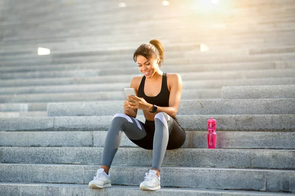 Menina preta desportiva em usar o telefone enquanto descansa — Fotografia de Stock