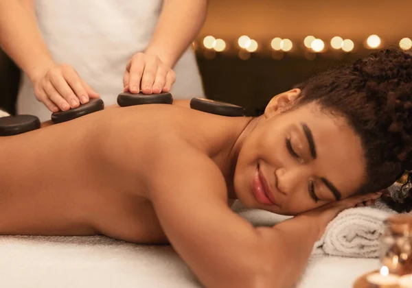 Спа-терапевт делает массаж горячими камнями для черной женщины — стоковое фото