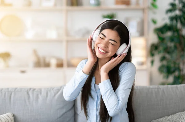 好きな歌。自宅でワイヤレスヘッドフォンで音楽を聴く楽しいアジアの女の子 — ストック写真