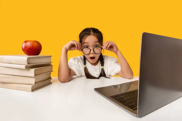 Fantastiska skolflicka tittar på kameran sitter på laptop, gul bakgrund — Stockfoto