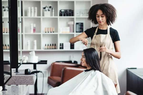 Mujer joven disfrutando de corte de pelo en el salón de belleza con maestro negro —  Fotos de Stock