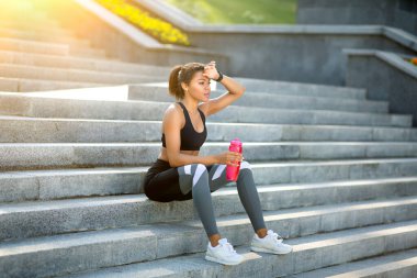 Bitkin siyah kız koşucu parkta merdivenlerde dinleniyor.