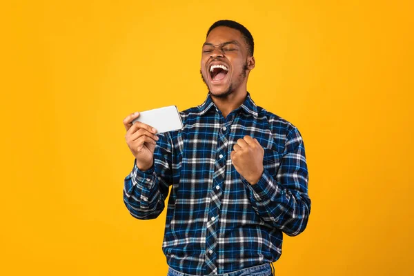 Vreugdevolle zwarte man met een smartphone schreeuwen schuddende vuisten in de studio — Stockfoto