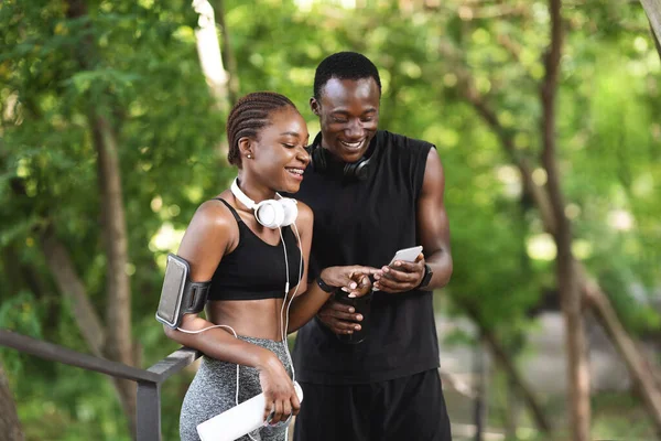 Casal preto animado verificando chamadas queimadas após o treinamento ao ar livre com aplicativo Smartphone — Fotografia de Stock