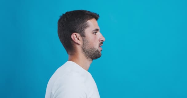 Young man using inhaler, blue studio background, side view — Stock Video