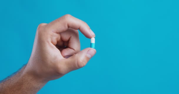 Masculino mão segurando cápsula pílula na mão, azul estúdio fundo — Vídeo de Stock