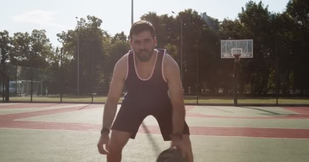 Молодой баскетболист капает мяч между ног на открытой площадке — стоковое видео