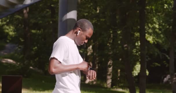 Αφροαμερικάνος με ακουστικά που ελέγχει τη δραστηριότητά του στο SmartWatch — Αρχείο Βίντεο