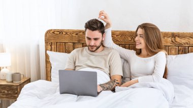 Aile, evde bir akşam ve flört. Dizüstü bilgisayarda çalışan genç bir adam, gülümseyen karısı saçlarına dokunuyor.
